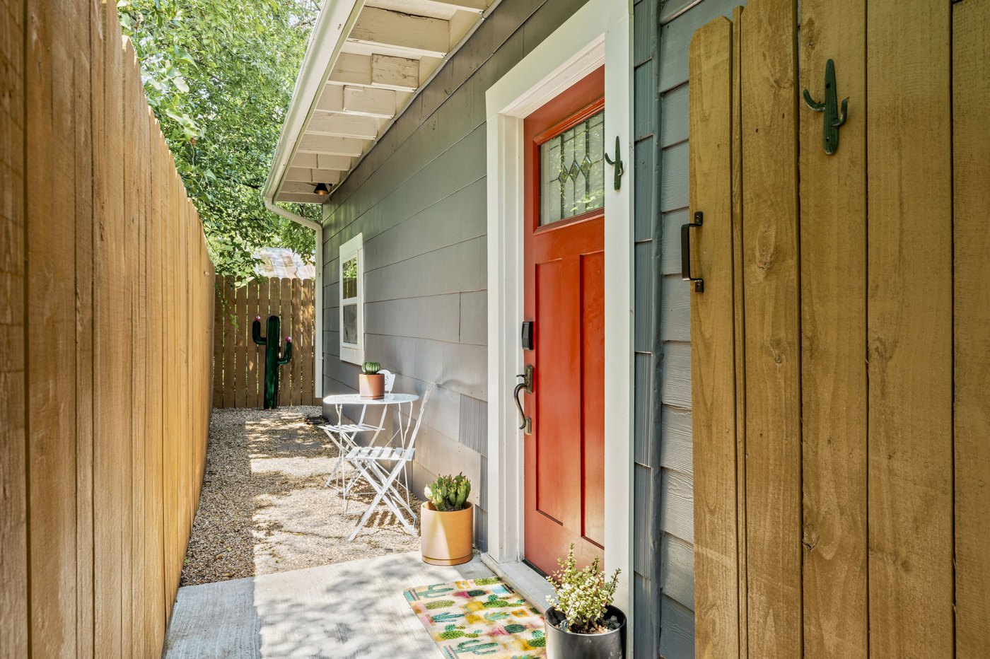 The red front door of a backyard rental unit, with a bistro table in the side yard